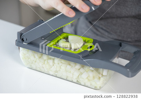 Modern kitchen vegetable chopper, operated by a person's hands, efficiently dices fresh onion into uniform cubes, simplifying quick meal preparation Modern kitchen vegetable chopper, operated by a person's hands, efficiently dices fresh onion into uniform cubes, simplifying quick meal preparation 128822938
