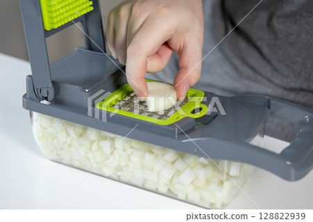 Hand operates a multi-functional kitchen food chopper, efficiently dicing fresh onion for quick, convenient meal preparation and home cooking Hand operates a multi-functional kitchen food chopper, efficiently dicing fresh onion for quick, convenient meal preparation and home cooking 128822939