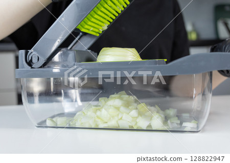 A person utilizes an innovative kitchen vegetable chopper to quickly dice a fresh onion, illustrating efficient food preparation for healthy home cooking and convenience 128822947