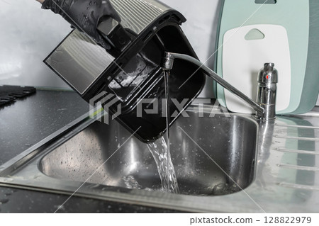 Hand in black glove cleans air fryer basket under running water in kitchen sink, emphasizing appliance maintenance and home cleanliness Hand in black glove cleans air fryer basket under running water in kitchen sink, emphasizing appliance maintenance and home cleanliness 128822979