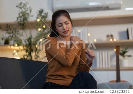 Health Awareness: Young woman experiencing shoulder pain at home Health Awareness: Young woman experiencing shoulder pain at home 128823251
