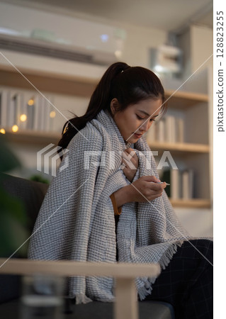 Self-Care. Young woman feeling cold and checking her health with a thermometer. 128823255