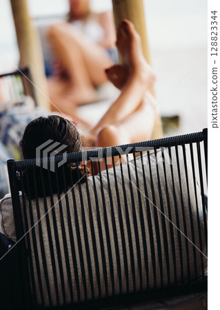 A young woman in a bright orange swimsuit relaxes at a table in a summer bar A young woman in a bright orange swimsuit relaxes at a table in a summer bar 128823344