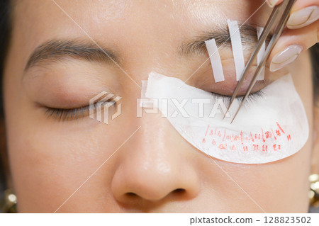 Young southeast asian woman at beauty salon for an eyelashes extension procedure. calm female seeks natural beauty focusing on eyes health wellness and professional makeup 128823502