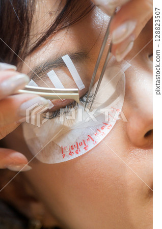 Relaxed young southeast asian woman during an eyelashes extension procedure in beauty salon. female enhances natural beauty for eyes part of health and wellness makeup routine 128823507