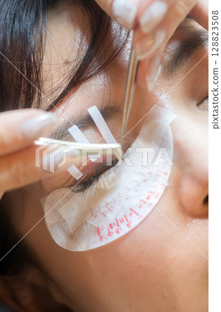 Young southeast asian woman in beauty salon getting an eyelashes extension procedure. calm female client focuses on natural beauty for eyes, health, wellness and makeup 128823508