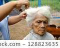 A caregiver is giving a haircut to an elderly woman. 128823635