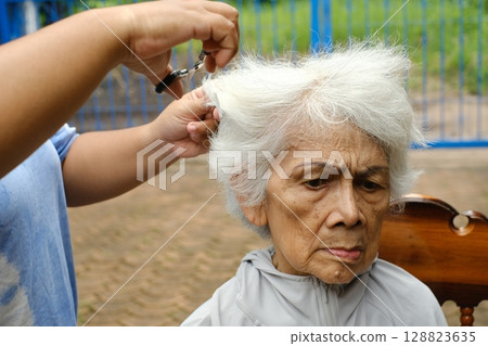A caregiver is giving a haircut to an elderly woman. 128823635