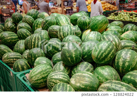 A pile of watermelons in a market. The watermelons are green and are piled on top of each other 128824022