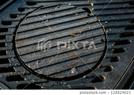 A black grill grate with a hole in the middle. The grate is dirty and has some food particles on it. 128824023
