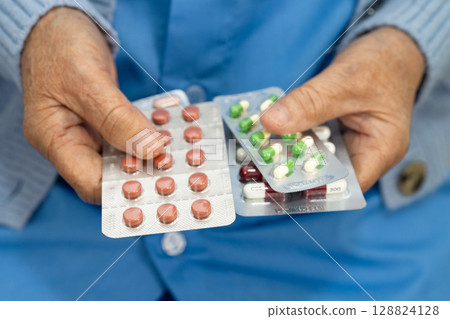 Asian senior woman patient holding antibiotics capsule pills for treatment infection patient in hospital, Pharmacy drugstore concept. Asian senior woman patient holding antibiotics capsule pills for treatment infection patient in hospital, Pharmacy drugstore concept. 128824128
