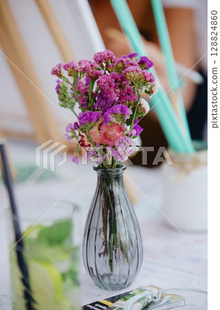 Fresh wild flowers stand in a glass vase on the table. In the background a glass Fresh wild flowers stand in a glass vase on the table. In the background a glass 128824860