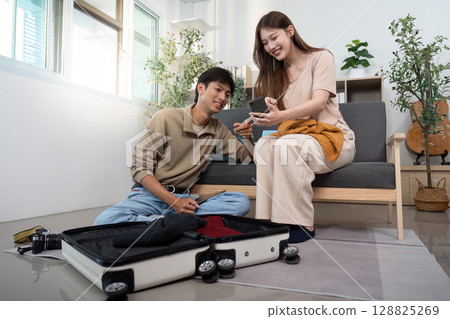Couple sharing travel plans while packing sweaters Couple sharing travel plans while packing sweaters 128825269
