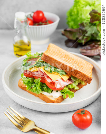 Sandwich of toast bread with bacon, cheese, tomatoes, lettuce, arugula and sauce in a plate  128825694