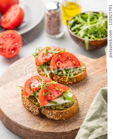 Healthy sesame toast with tomatoes, mozzarella, arugula, pesto on wooden board on light background Healthy sesame toast with tomatoes, mozzarella, arugula, pesto on wooden board on light background 128825701