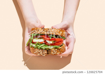 Hands holding sandwich of grain bread with tomatoes, mozzarella, arugula and pesto Hands holding sandwich of grain bread with tomatoes, mozzarella, arugula and pesto 128825704