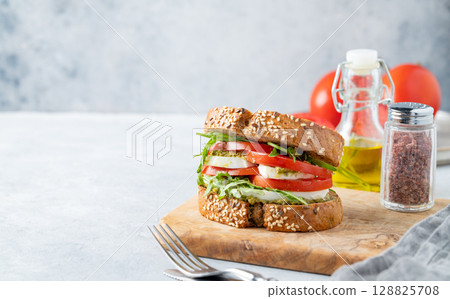 Sandwich of grain bread with tomatoes, mozzarella, arugula and pesto on a wooden board Sandwich of grain bread with tomatoes, mozzarella, arugula and pesto on a wooden board 128825708