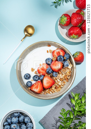 Natural yogurt with granola, blueberry and strawberry in a bowl on a blue  background with spoon 128825715