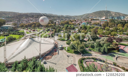 Aerial timelapse of Rike Park, a modern urban park in Tbilisi's Old Town with green trees and lawns. The Bridge of Peace in the background. Georgia 128826208