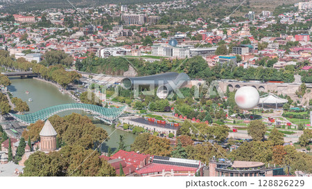 Aerial timelapse of Rike Park, a modern urban park in Tbilisi's Old Town with green trees and lawns. The Bridge of Peace in the background. Georgia 128826229