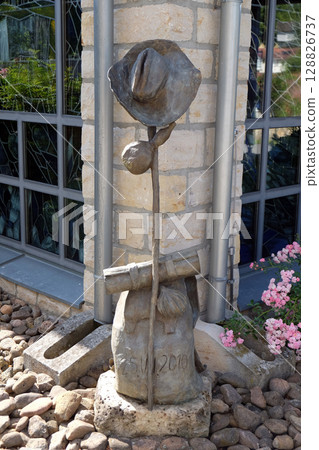 Hat, stick and backpack, symbols of pilgrims in Santiago de Compostela by Sieger Koder in front of Church of Saint Bartholomew in Leutershausen, Germany 128826737