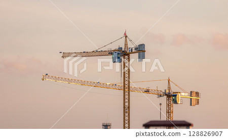 Large construction site including several cranes working on a building complex, with golden sky during sunset timelapse. Large construction site including several cranes working on a building complex, with golden sky during sunset timelapse. 128826907