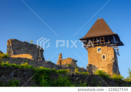 nevytske, ukraine - 19 may, 2018: castle with tower and stone wall at sunset. medieval fortress architecture of ukraine. travel destination and heritage site of transcarpathia nevytske, ukraine - 19 may, 2018: castle with tower and stone wall at sunset. medieval fortress architecture of ukraine. travel destination and heritage site of transcarpathia 128827334