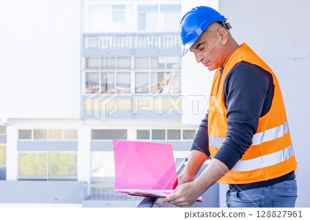 Absorbed construction engineer or building contractor wearing a blue protective helmet checking office blueprints. Copy space 128827961