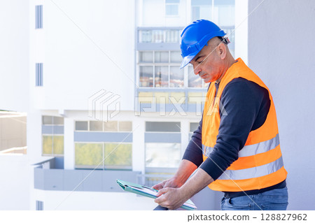 Absorbed construction engineer or building contractor wearing a blue protective helmet checking office blueprints. Copy space Absorbed construction engineer or building contractor wearing a blue protective helmet checking office blueprints. Copy space 128827962