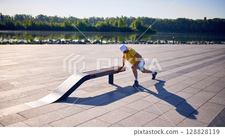 Senior man doing side lunges using bench on urban riverside promenade 128828119