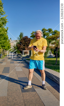 Smiling senior man using smartphone while wearing headphones during outdoor walk 128828130