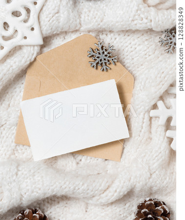 Blank card over envelope on white knitted sweater near Christmas decor, winter Holiday mockup 128828349
