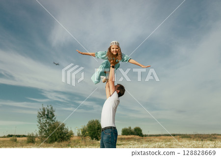 Father lifting daughter in air in field on sunny day 128828669