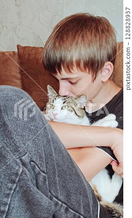 Teenage boy and a cat. Handsome guy hugs his cat while sitting on the couch. Vertical Teenage boy and a cat. Handsome guy hugs his cat while sitting on the couch. Vertical 128828937