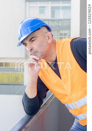 Portrait of an engineer wearing protective workwear posing looking at an unspecified point leaning chin on hand 128829024