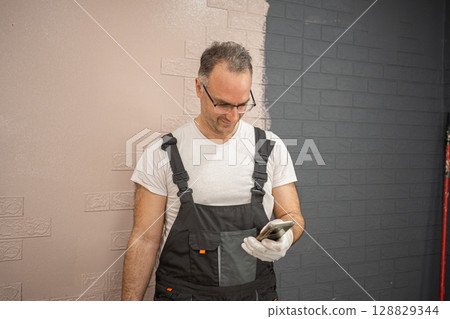 Man in Overalls Painting Brick Wall 128829344