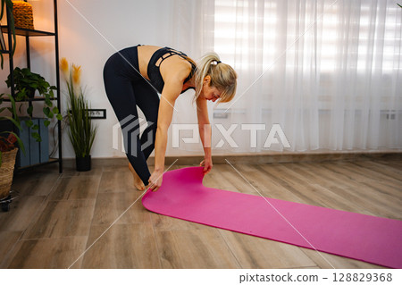 Stretching out a vibrant yoga mat in a serene home environment 128829368