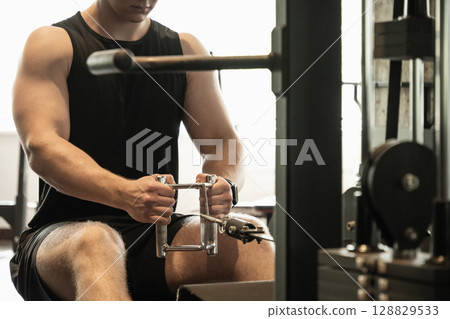 Young caucasian man wearing blank sleeveless tank top exercising on rowing machine at gym. Close up. Young caucasian man wearing blank sleeveless tank top exercising on rowing machine at gym. Close up. 128829533
