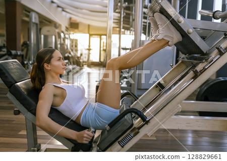 Beautiful woman sporty girl exercising using leg press machine at the gym 128829661