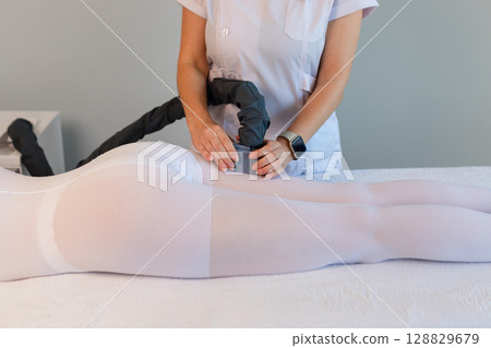 Woman in special white suit getting anti cellulite massage in a spa salon. LPG, and body contouring treatment in clinic.Reset body weight with LPG massage. Woman in special white suit getting anti cellulite massage in a spa salon. LPG, and body contouring treatment in clinic.Reset body weight with LPG massage. 128829679