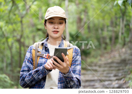 Young Woman Using Smartphone While Hiking in Forest 128829703