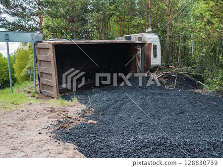 A truck has tipped over, spilling asphalt across the roadside near a forest A truck has tipped over, spilling asphalt across the roadside near a forest 128830739