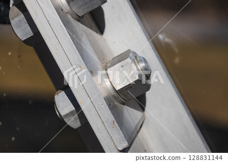 Close up of stainless steel bolt and nut securing angled beam plate in industrial structure 128831144