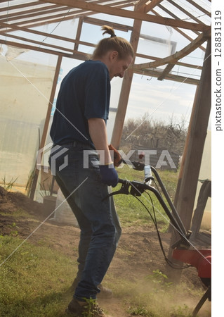 Young man engaged in household chores and small-scale rural farming, tending to his garden with care and dedication. His daily routine reflects a sustainable and self-sufficient way of life Young man engaged in household chores and small-scale rural farming, tending to his garden with care and dedication. His daily routine reflects a sustainable and self-sufficient way of life 128831319