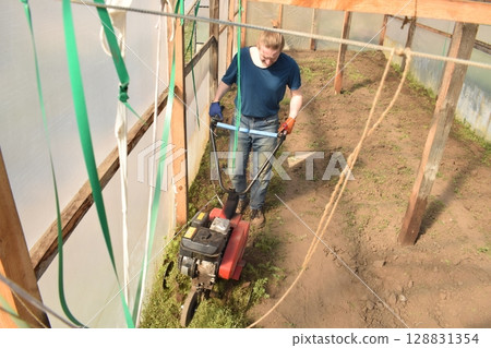 Young man engaged in household chores and small-scale rural farming, tending to his garden with care and dedication. His daily routine reflects a sustainable and self-sufficient way of life Young man engaged in household chores and small-scale rural farming, tending to his garden with care and dedication. His daily routine reflects a sustainable and self-sufficient way of life 128831354