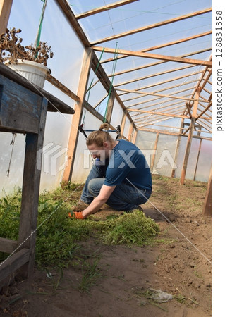 Young man engaged in household chores and small-scale rural farming, tending to his garden with care and dedication. His daily routine reflects a sustainable and self-sufficient way of life Young man engaged in household chores and small-scale rural farming, tending to his garden with care and dedication. His daily routine reflects a sustainable and self-sufficient way of life 128831358