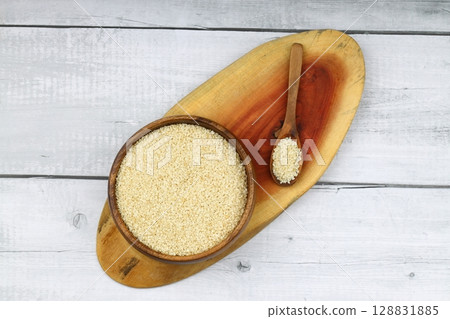 Top view closeup of freshly harvested white sesame in wooden bowl isolated on wooden background with clipping path. 128831885
