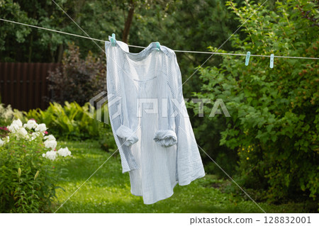 Clean white striped shirt on clothesline outdoors to dry in summer garden. Sustainable Life. Household Chores Clean white striped shirt on clothesline outdoors to dry in summer garden. Sustainable Life. Household Chores 128832001