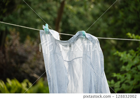 Clean white striped shirt on clothesline outdoors to dry in summer garden. Close up. Household Chores Clean white striped shirt on clothesline outdoors to dry in summer garden. Close up. Household Chores 128832002