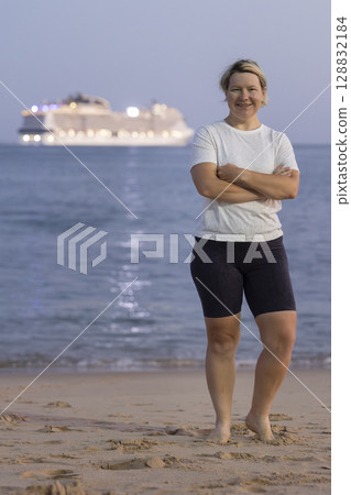 Tourist smiling with arms crossed on beach at dusk with cruise ship in background Tourist smiling with arms crossed on beach at dusk with cruise ship in background 128832184